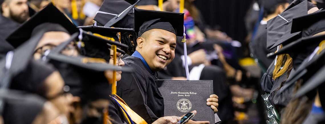 A graduate holding his recently awarded degree at ACC commencement ceremony