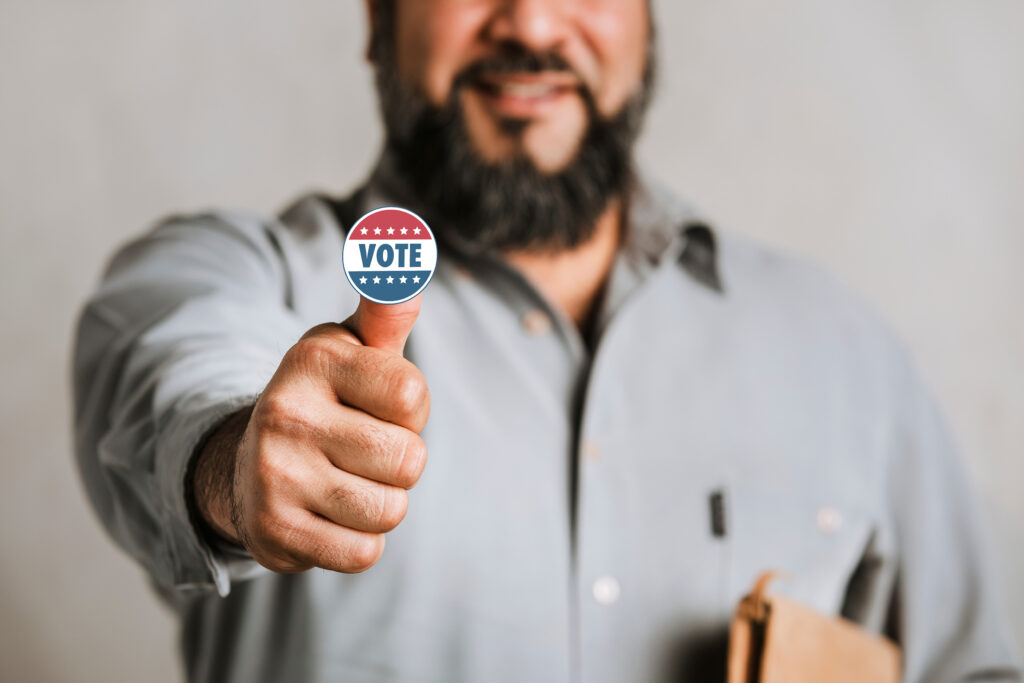 Man with hand in thumbs-up position with Vote sticker on the end of extended thumb.